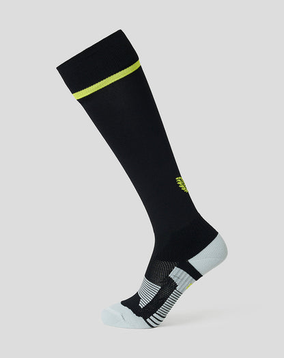 A single knee-high athletic sock in black with a bright neon yellow-green accent band near the cuff, a small matching accent on the side, and a light gray toe and heel, shown on a plain light gray background.
