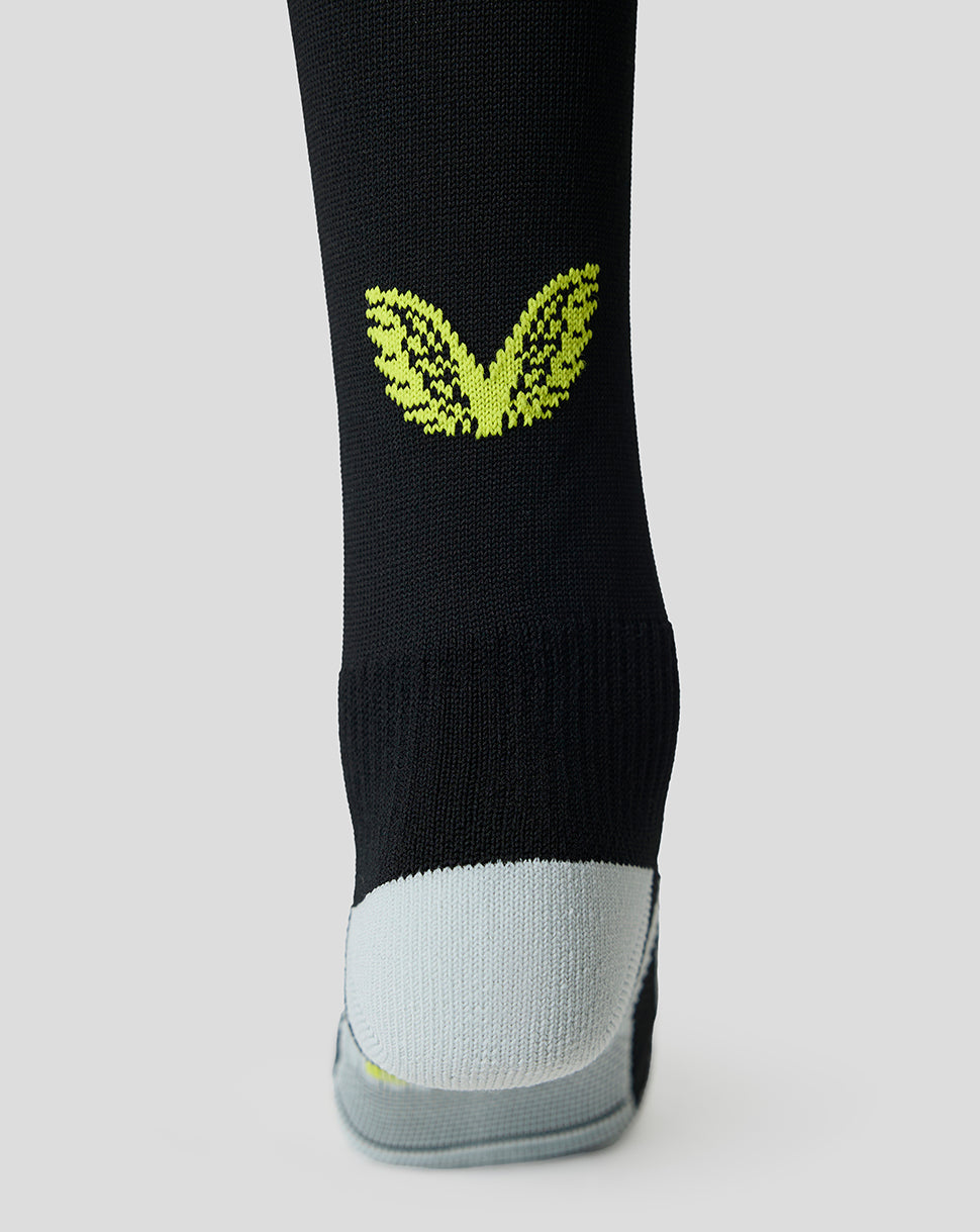 A close-up of a black athletic sock with a bright lime green butterfly graphic on the calf and a light gray toe section, shown against a neutral light gray background.