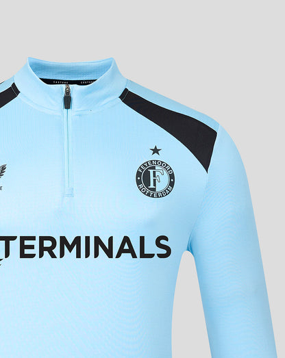Close up of the light blue training midlayer front showing crest with star, zipper collar, and sponsor logo