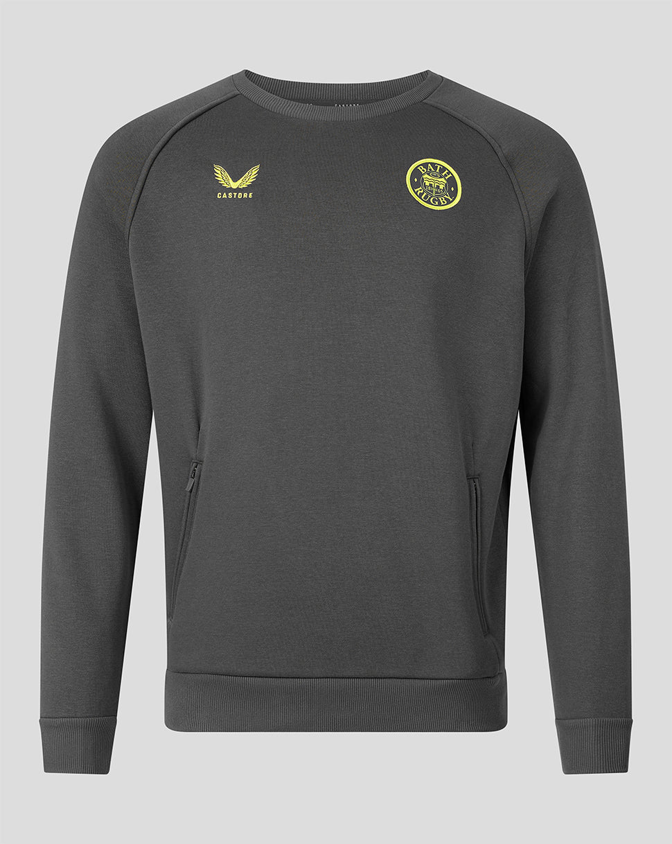 A dark gray crewneck sweatshirt with yellow embroidered accents, featuring the Castore logo on the right chest and a circular club crest on the left chest, displayed on a solid gray background.
