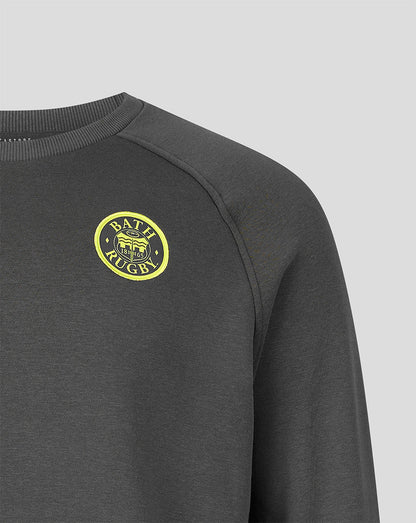 Close-up of a dark gray crewneck sweatshirt featuring a yellow circular 'BATH Rugby' logo on the left chest, set against a light gray background.