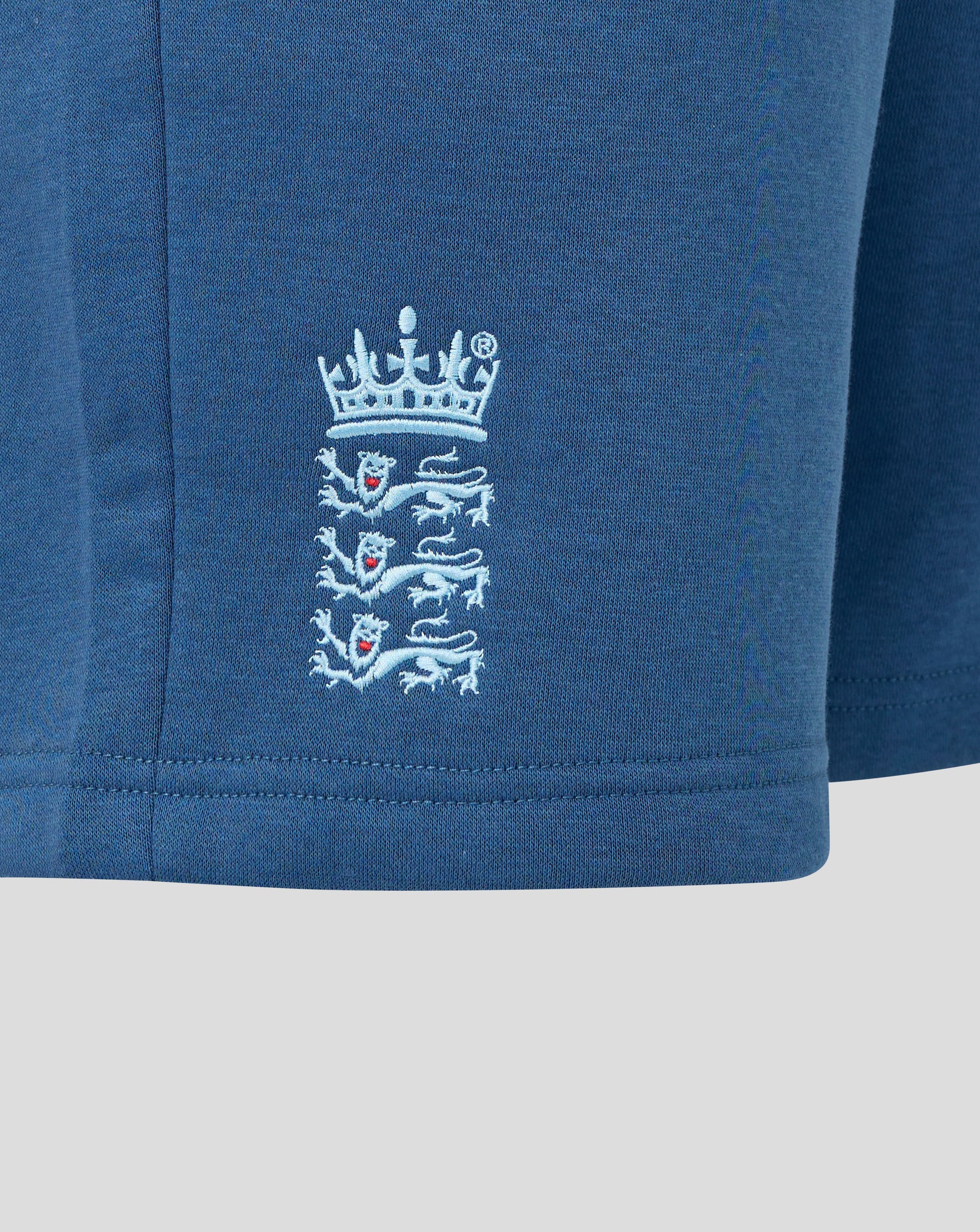 Close-up of a blue garment with a white embroidered logo on a light gray background