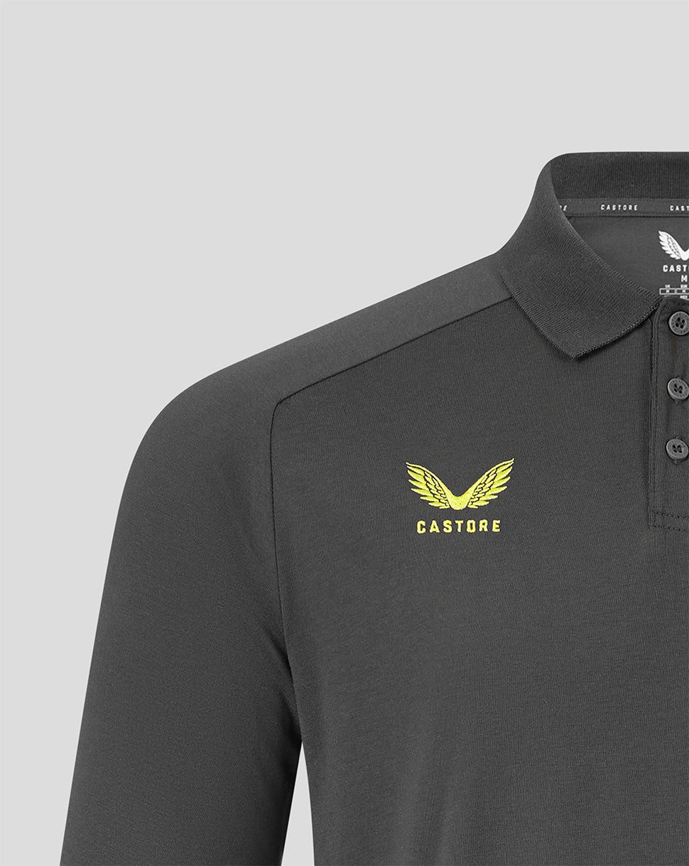 Close-up of a dark gray Castore polo shirt featuring a yellow embroidered winged logo and the brand name 'CASTORE' on the left chest, set against a light gray background.