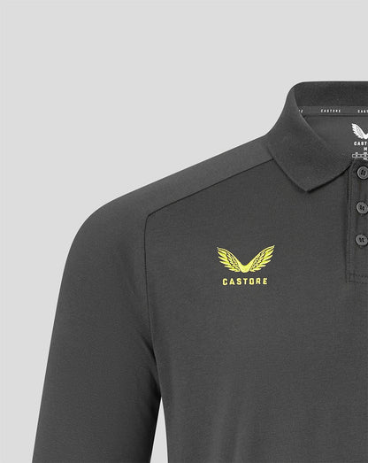 Close-up of a dark gray Castore polo shirt featuring a yellow embroidered winged logo and the brand name 'CASTORE' on the left chest, set against a light gray background.