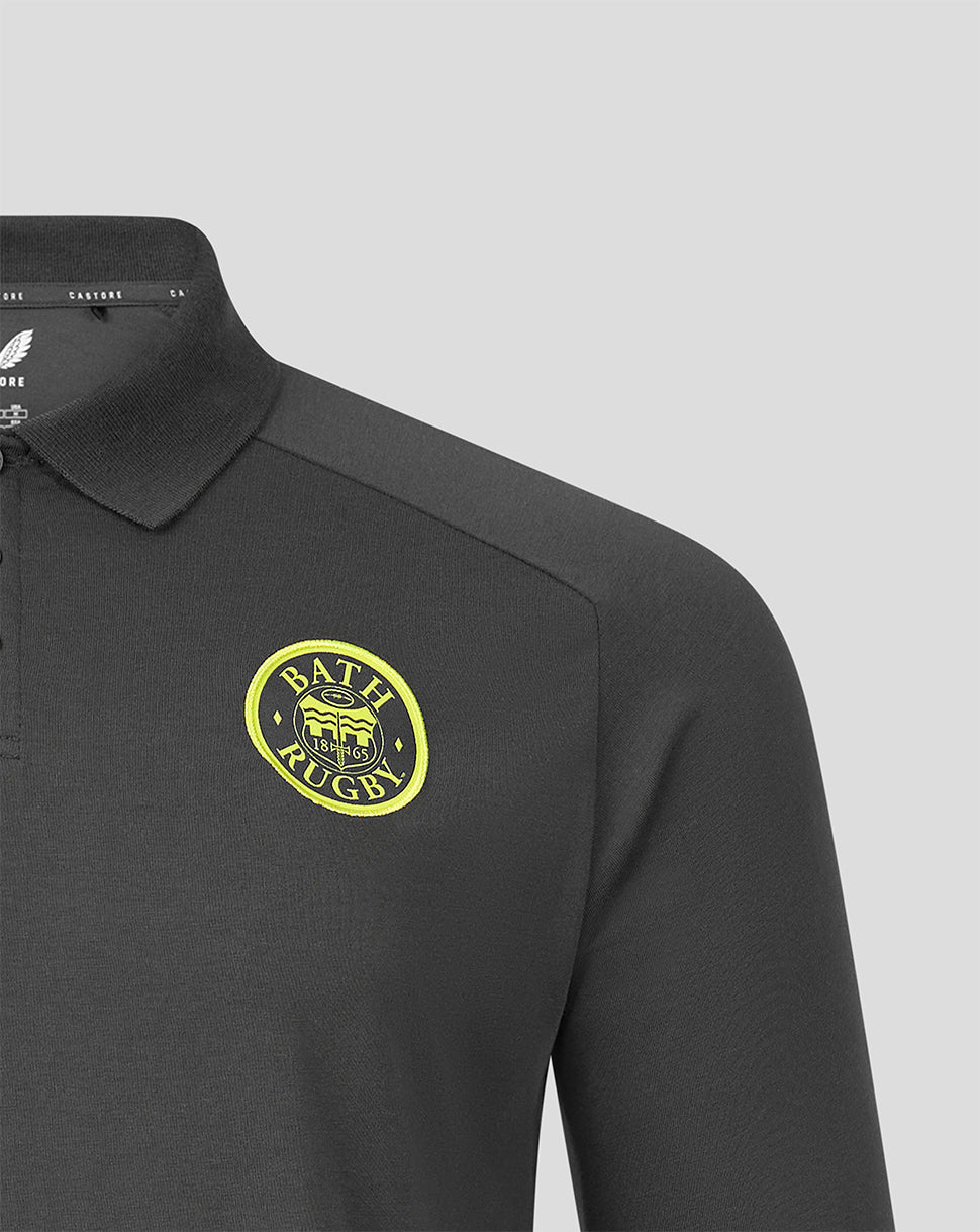 Close-up of a dark gray long-sleeve polo shirt with a yellow and black Bath Rugby crest on the left chest, set against a solid light gray background.