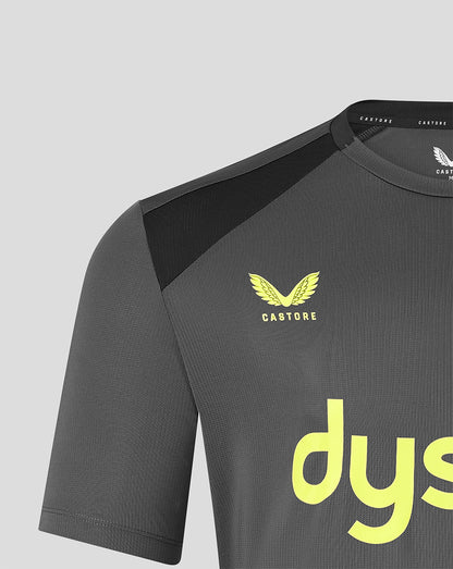 Close-up of a dark gray athletic jersey with a black shoulder panel, a yellow Castore wing logo on the chest, and a large yellow sponsor logo on the front, shown against a light gray background.