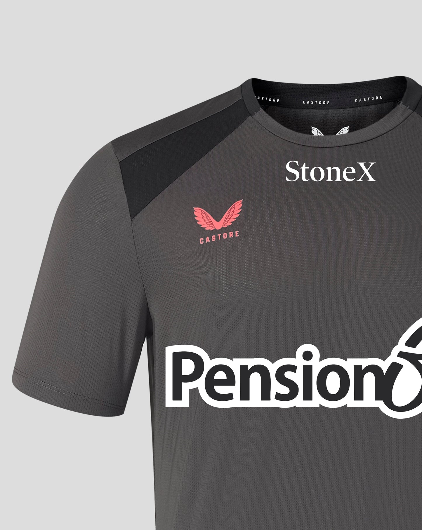 A close-up of a dark gray Castore athletic jersey with black shoulder panels, featuring the Castore wing logo in red, the StoneX sponsor logo in white, and the Pensionbee sponsor logo across the front.