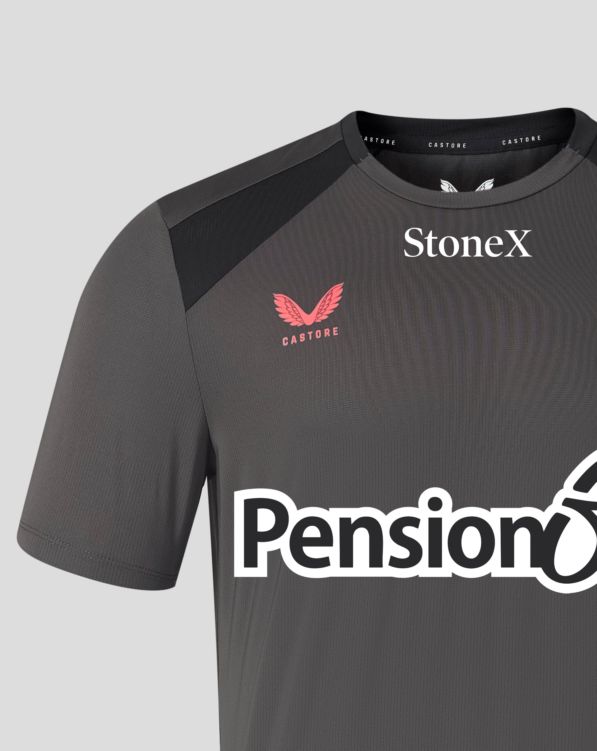 A close-up of a dark gray Castore athletic jersey with black shoulder panels, featuring the Castore wing logo in red, the StoneX sponsor logo in white, and the Pensionbee sponsor logo across the front.