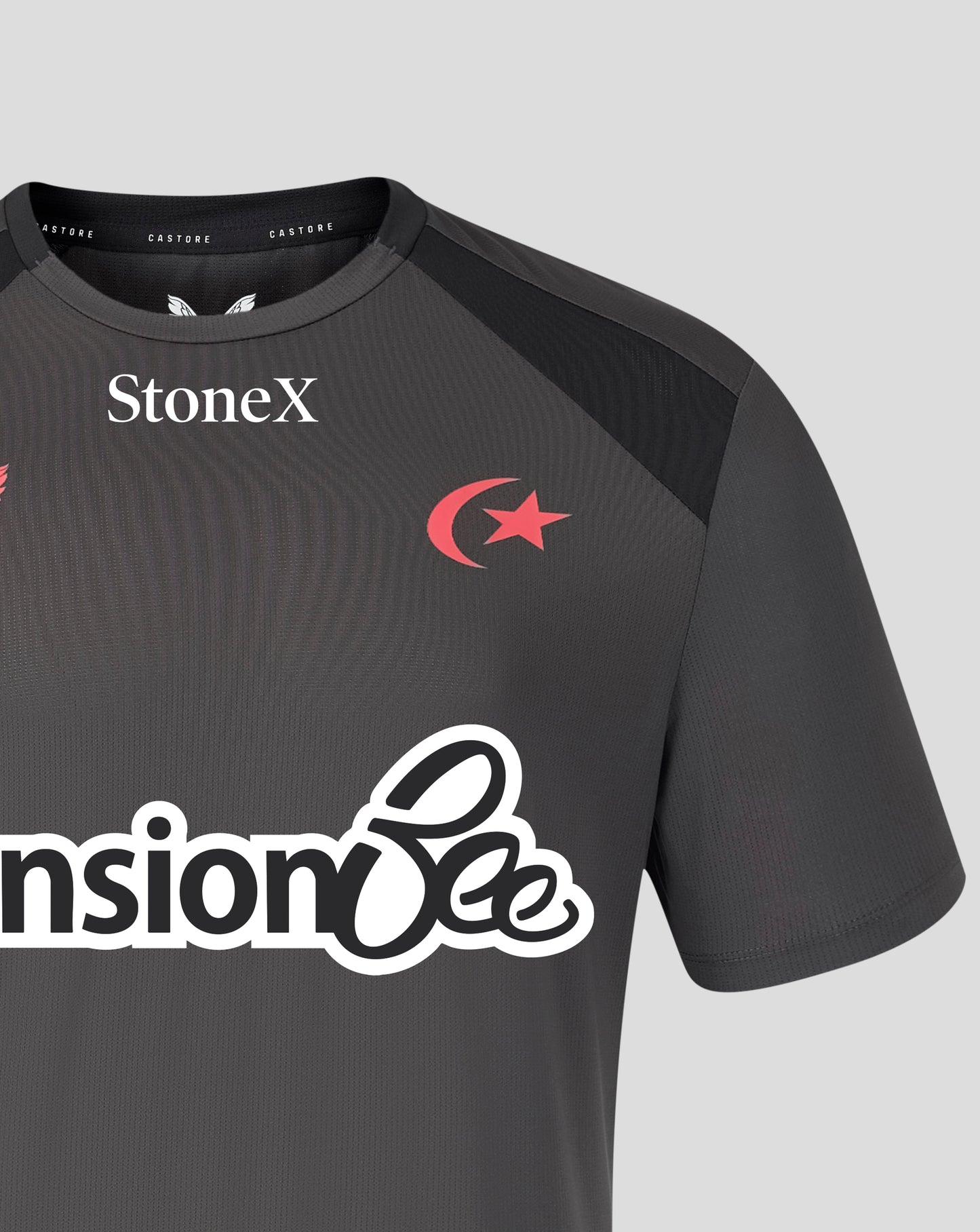 A close-up of a dark gray athletic jersey with black shoulder panels, featuring the StoneX logo in white on the chest, a red crescent and star emblem, and a large white sponsor logo across the front.