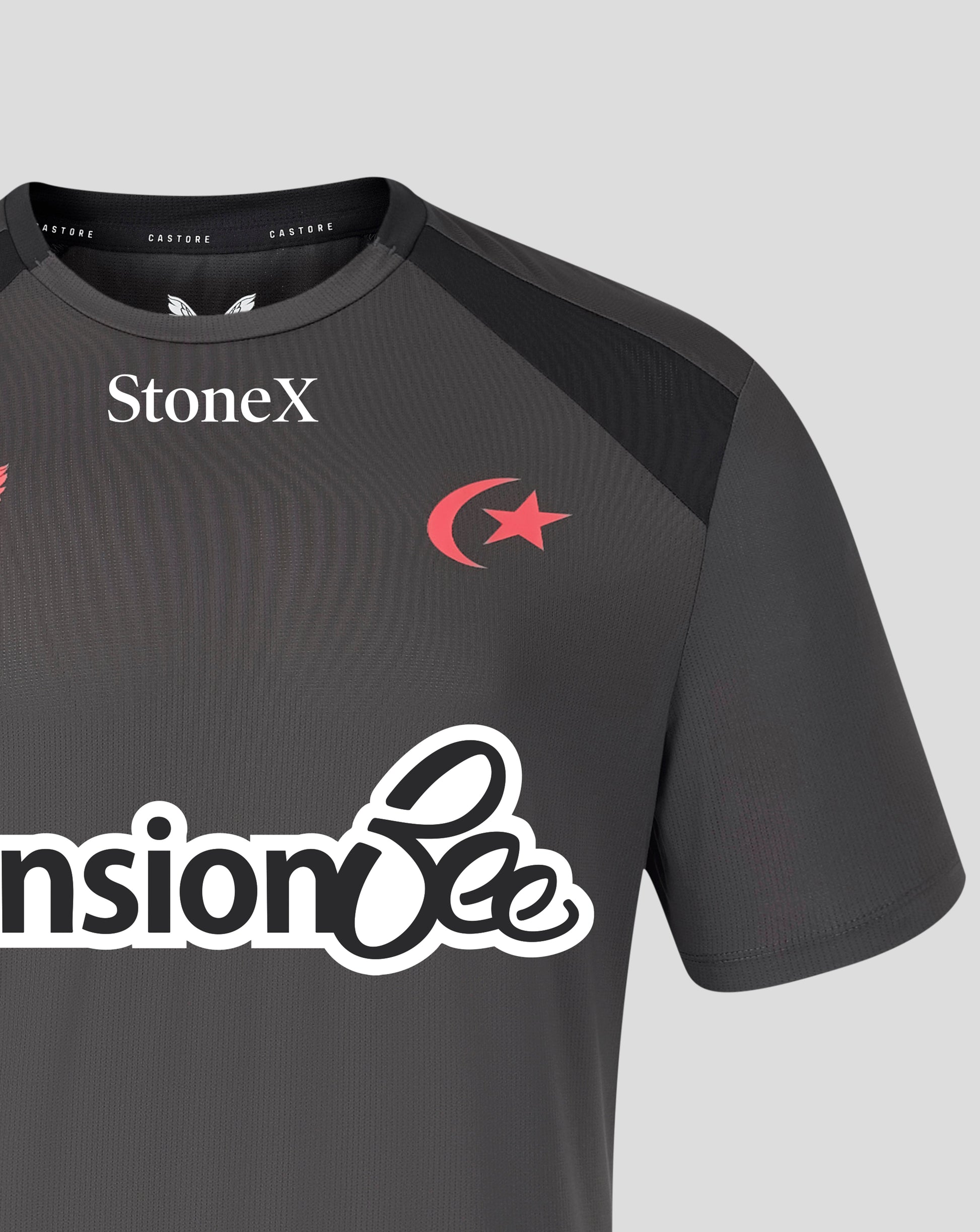 A close-up of a dark gray athletic jersey with black shoulder panels, featuring the StoneX logo in white on the chest, a red crescent and star emblem, and a large white sponsor logo across the front.