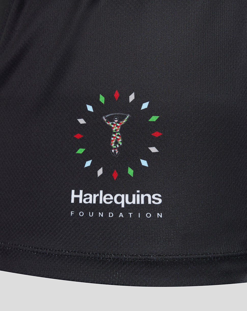 Close-up of a black athletic top featuring the Harlequins Foundation logo printed on the chest. The logo includes a central figure made of colorful dots, surrounded by small multicolored diamond shapes, with 'Harlequins FOUNDATION' printed in white below.