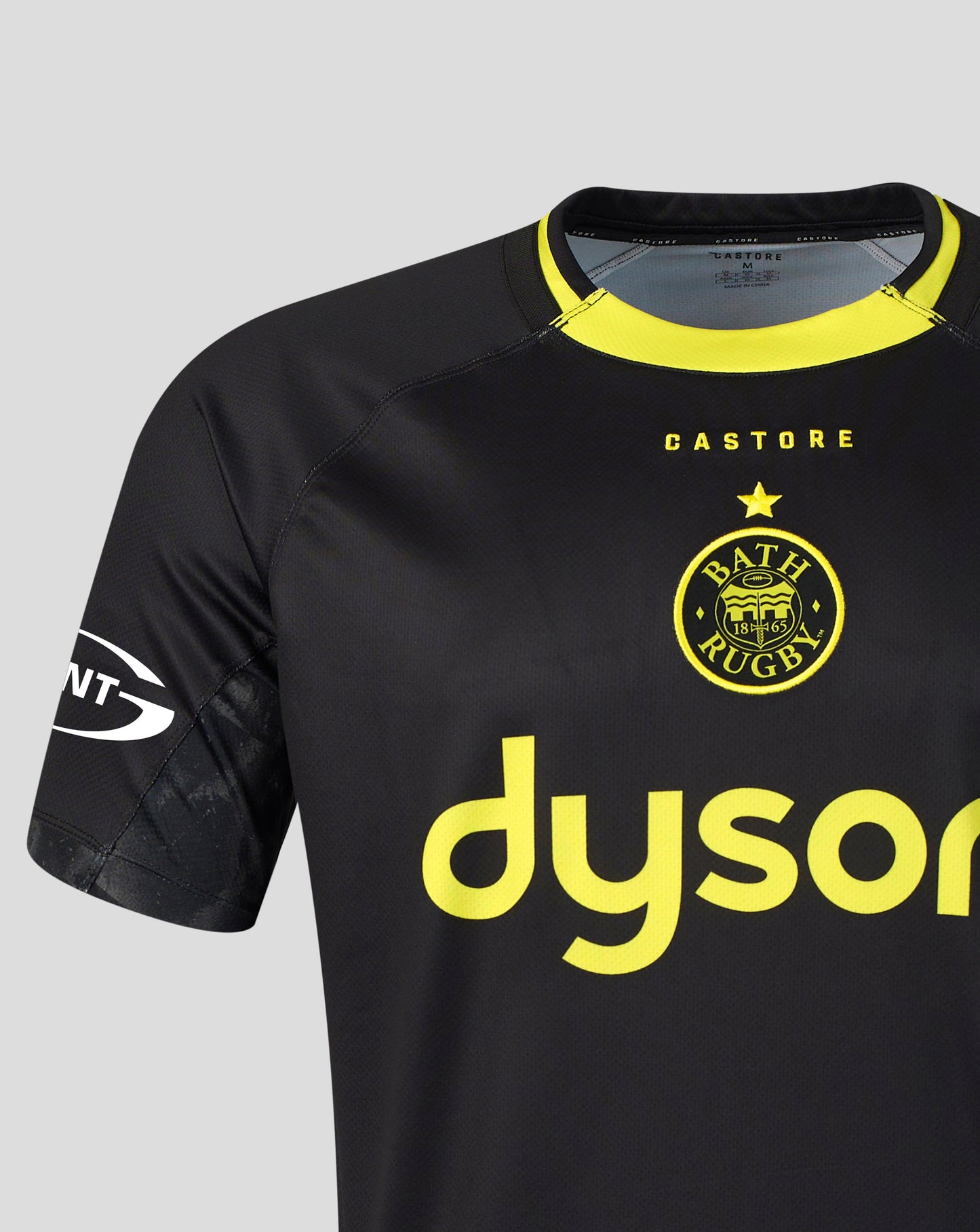 A close-up of a Bath Rugby football jersey in black with bright yellow accents, featuring the club's crest and a large 'dyson' sponsor logo on the front.