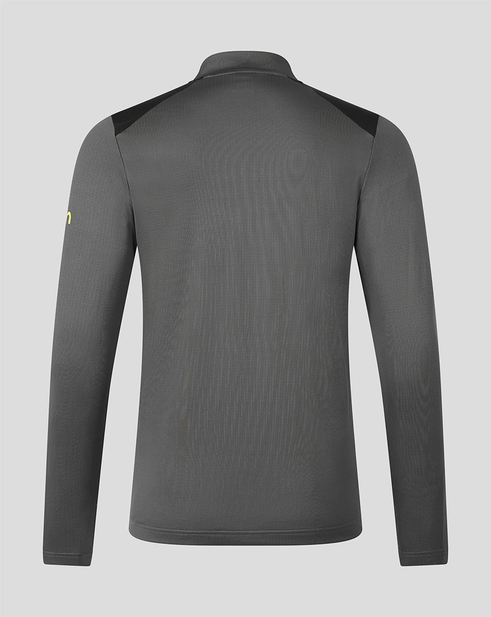 A dark gray long-sleeve athletic top shown from the back, featuring black shoulder panels and a small yellow logo on the left sleeve, set against a solid light gray background.