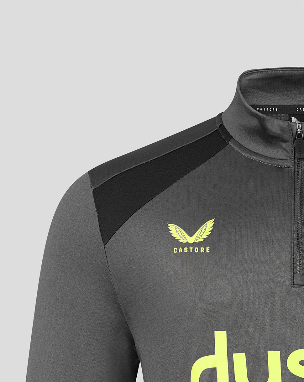 Close-up of a dark gray athletic quarter-zip top with black shoulder panels, a yellow Castore wing logo, and a partial yellow wordmark on a light gray background.