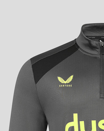 Close-up of a dark gray athletic quarter-zip top with black shoulder panels, a yellow Castore wing logo, and a partial yellow wordmark on a light gray background.