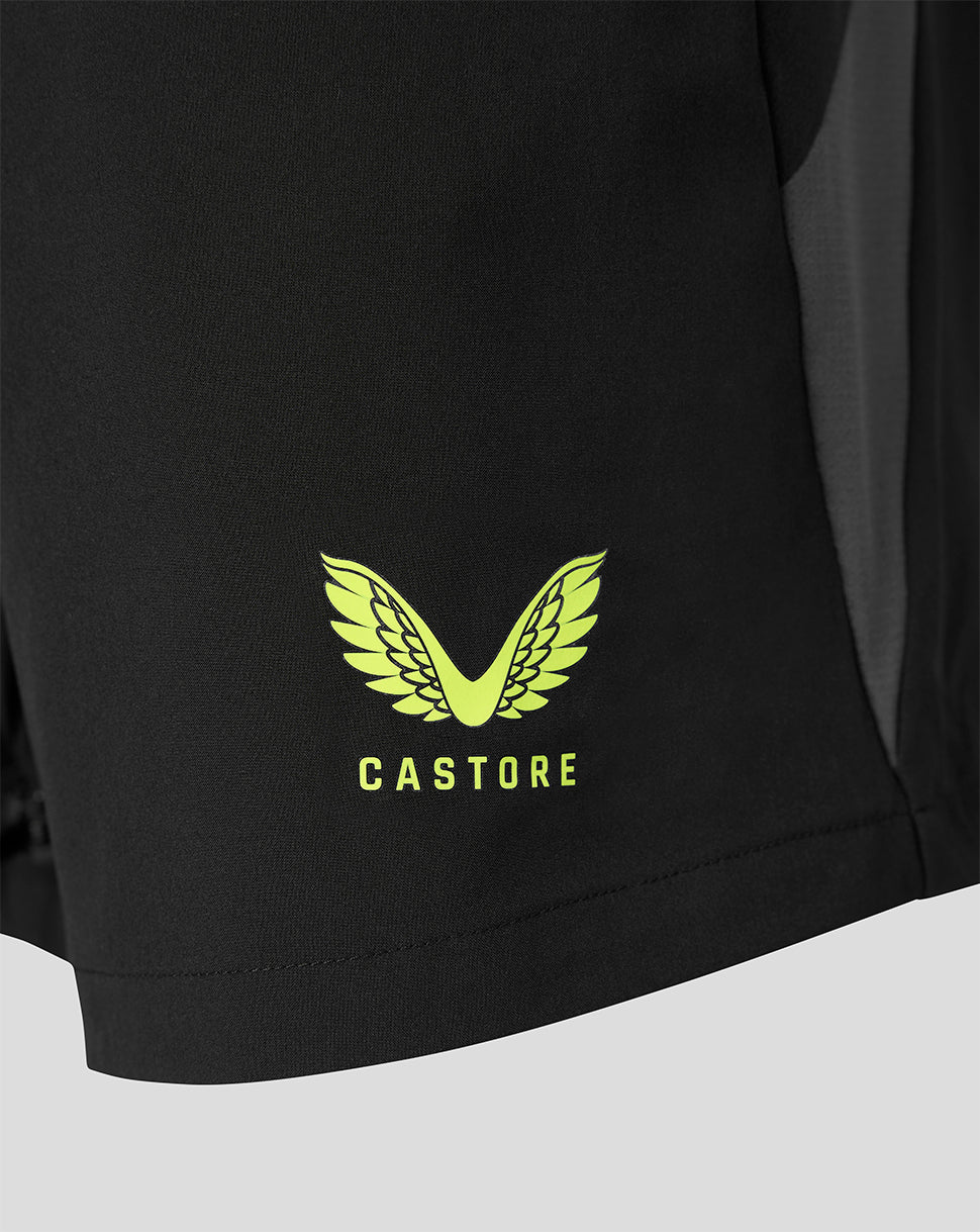 Close-up of a black athletic garment showing a bright yellow-green Castore wing logo and brand name printed on the lower front, with a dark side panel visible.