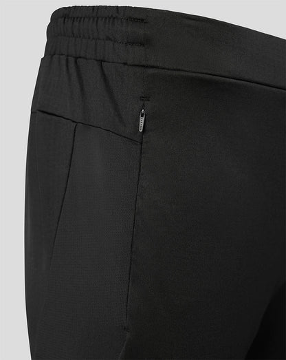 Close-up of black athletic pants showing the elastic waistband, side pocket seam, and a small vertical zip pocket with a silver zipper pull on a light gray background.