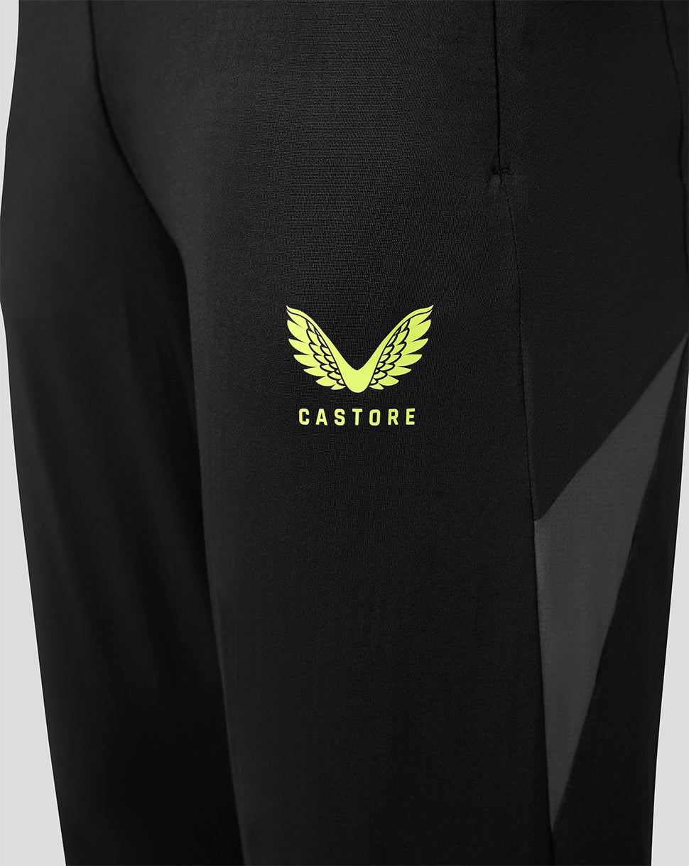 Close-up of black athletic pants featuring a bright yellow-green Castore wing logo and brand name on the thigh, with a sheer dark side panel.