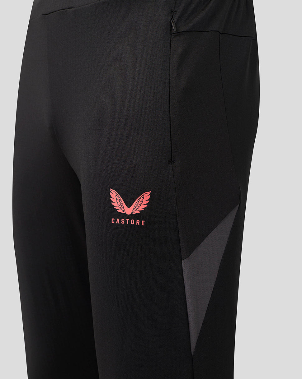 Close-up of black athletic pants with a pink Castore wing logo on the left thigh and a dark gray side panel, shown against a light gray background.