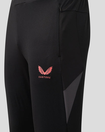 Close-up of black athletic pants with a pink Castore wing logo on the left thigh and a dark gray side panel, shown against a light gray background.