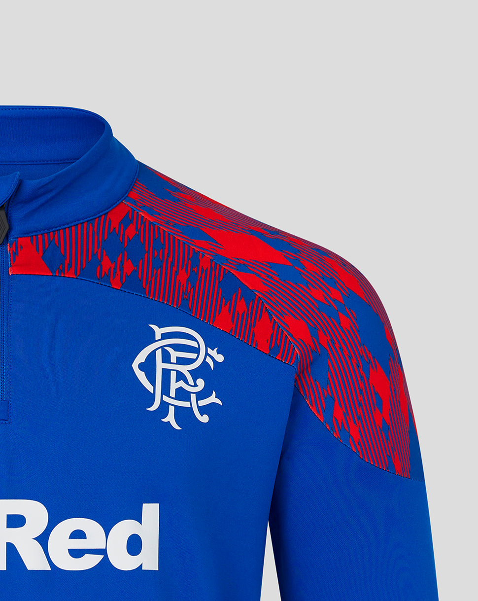 Close-up of a blue and red patterned athletic quarter-zip pullover with a white Rangers FC crest on the chest, shown against a light gray background.
