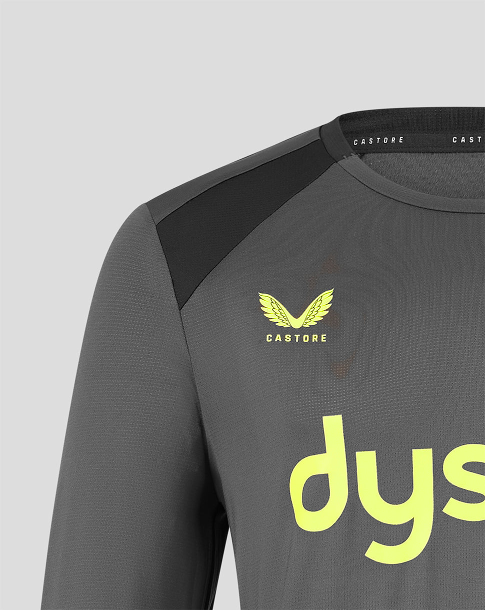 Close-up of a dark gray Castore athletic long-sleeve top with a black shoulder panel, a yellow winged logo with the word 'CASTORE' underneath, and a large yellow 'dys' logo on the front, set against a light gray background.