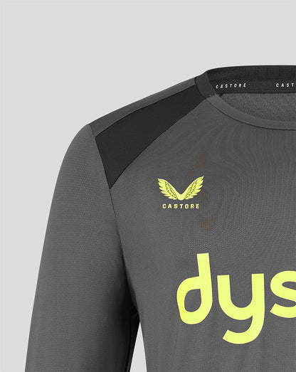 Close-up of a dark gray Castore athletic long-sleeve top with a black shoulder panel, a yellow winged logo with the word 'CASTORE' underneath, and a large yellow 'dys' logo on the front, set against a light gray background.