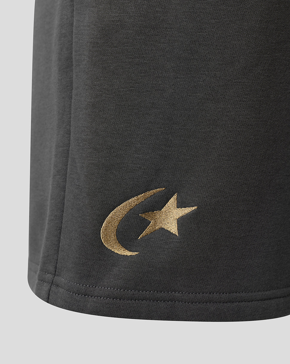 Close-up of a dark gray fabric garment showing a metallic gold embroidered crescent moon and star logo on the lower left side, set against a light gray background.