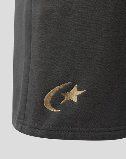 Close-up of a dark gray fabric garment showing a metallic gold embroidered crescent moon and star logo on the lower left side, set against a light gray background.