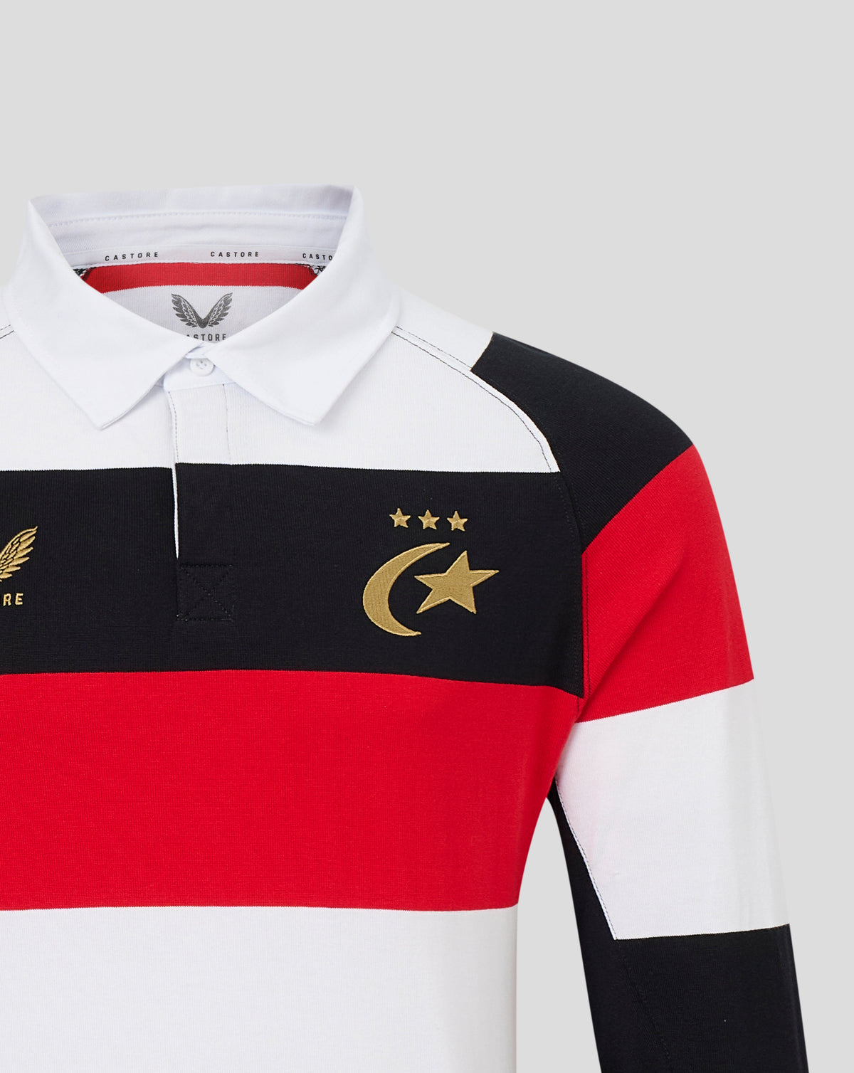 A close-up of a long-sleeve rugby shirt with horizontal color-blocked stripes in white, black, and red, featuring a gold crescent and star emblem with three stars on the left chest.