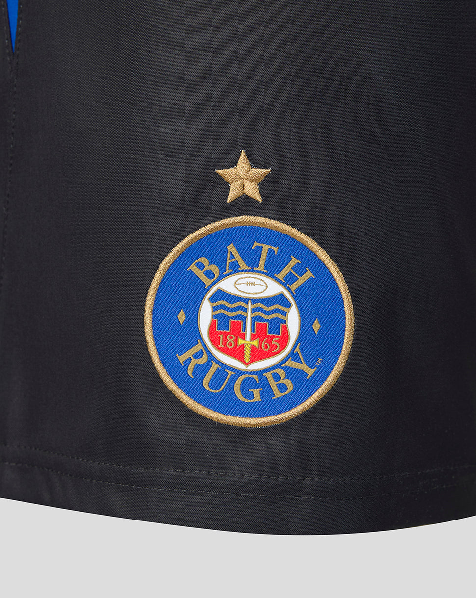 Close-up of a black athletic jersey or shorts fabric featuring an embroidered circular Bath Rugby crest in blue, gold, white, and red, with a gold star above it.