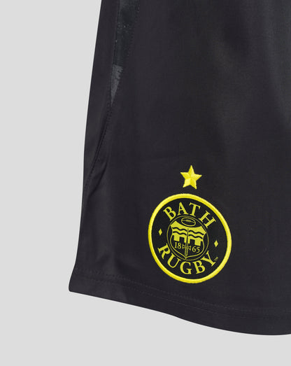 Close-up of a black athletic shorts leg featuring a yellow embroidered Bath Rugby club crest and star on the lower left side, set against a light gray background.