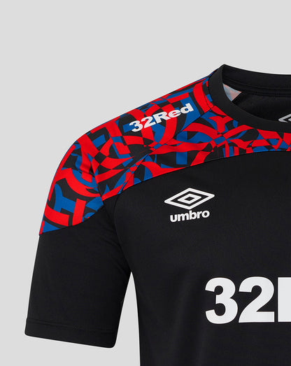 Close-up of a black short-sleeve soccer jersey with a red and blue geometric pattern on the shoulders and upper chest, white Umbro logo, and white '32Red' text on a light gray background.