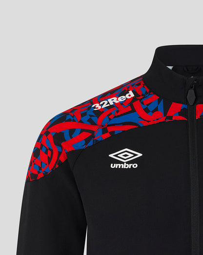 Close-up of a black zip-up jacket with a red and blue abstract patterned shoulder panel, white Umbro logo on the chest, and white 32Red text on the shoulder, shown against a light gray background.