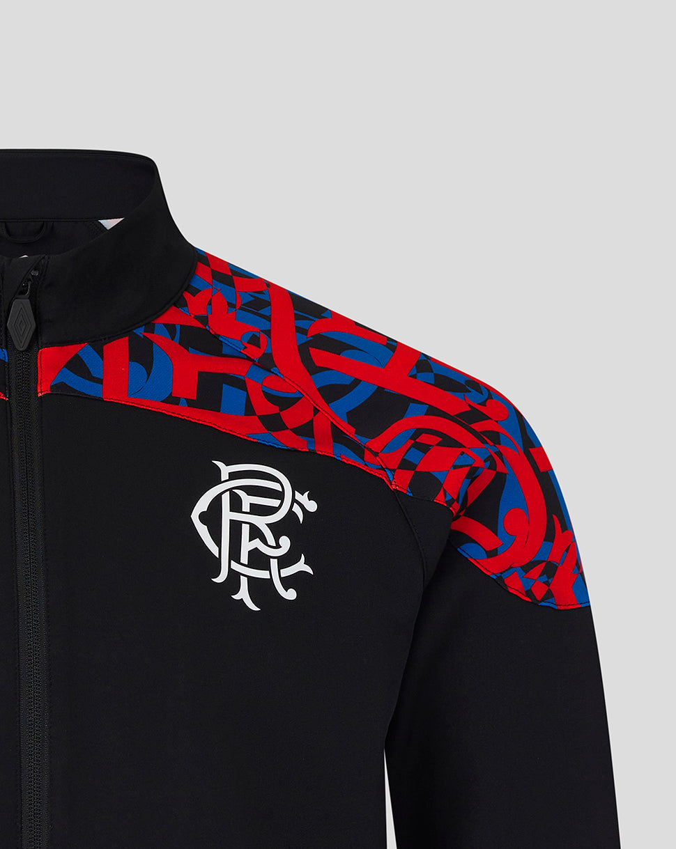 Close-up of a black zip-up jacket with a red and blue abstract patterned yoke and a white stylized 'R' crest on the chest, shown against a light gray background.