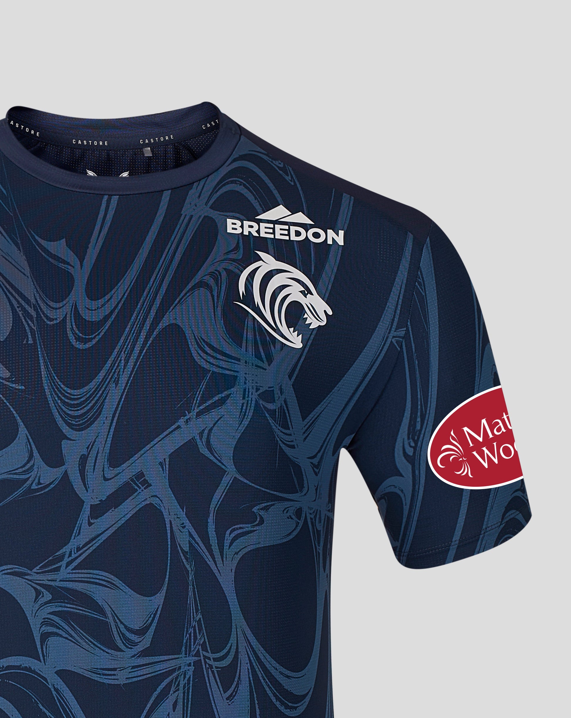 Close-up of a dark navy blue short-sleeve rugby jersey with a blue marbled pattern, featuring the white BREEDON logo and a red sponsor patch on the sleeve.