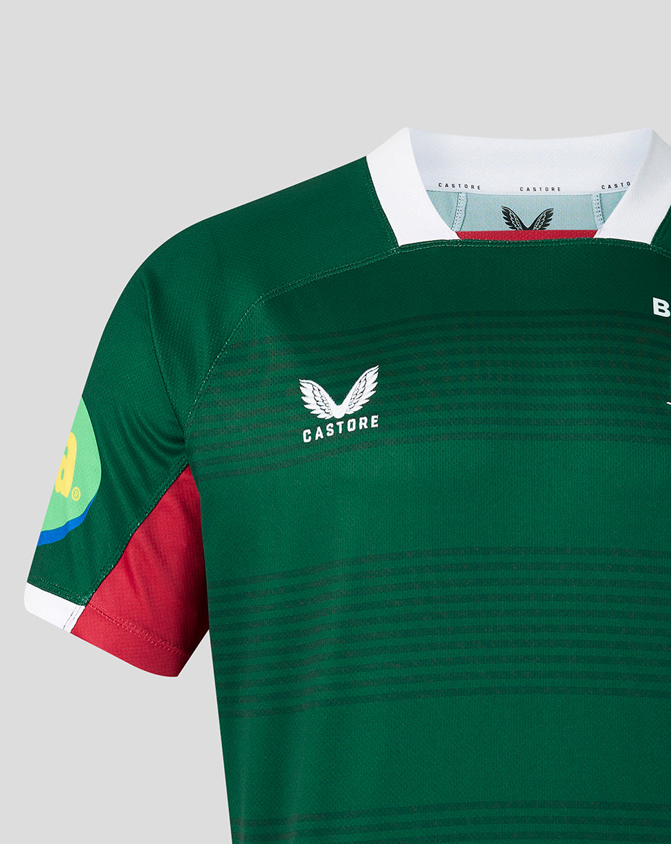 Close-up of a green Castore rugby jersey with a white collar, red side panel, and white wing logo on the chest, shown against a light gray background.