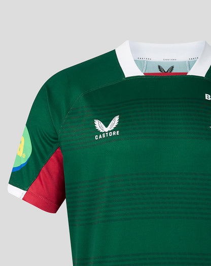 Close-up of a green Castore rugby jersey with a white collar, red side panel, and white wing logo on the chest, shown against a light gray background.