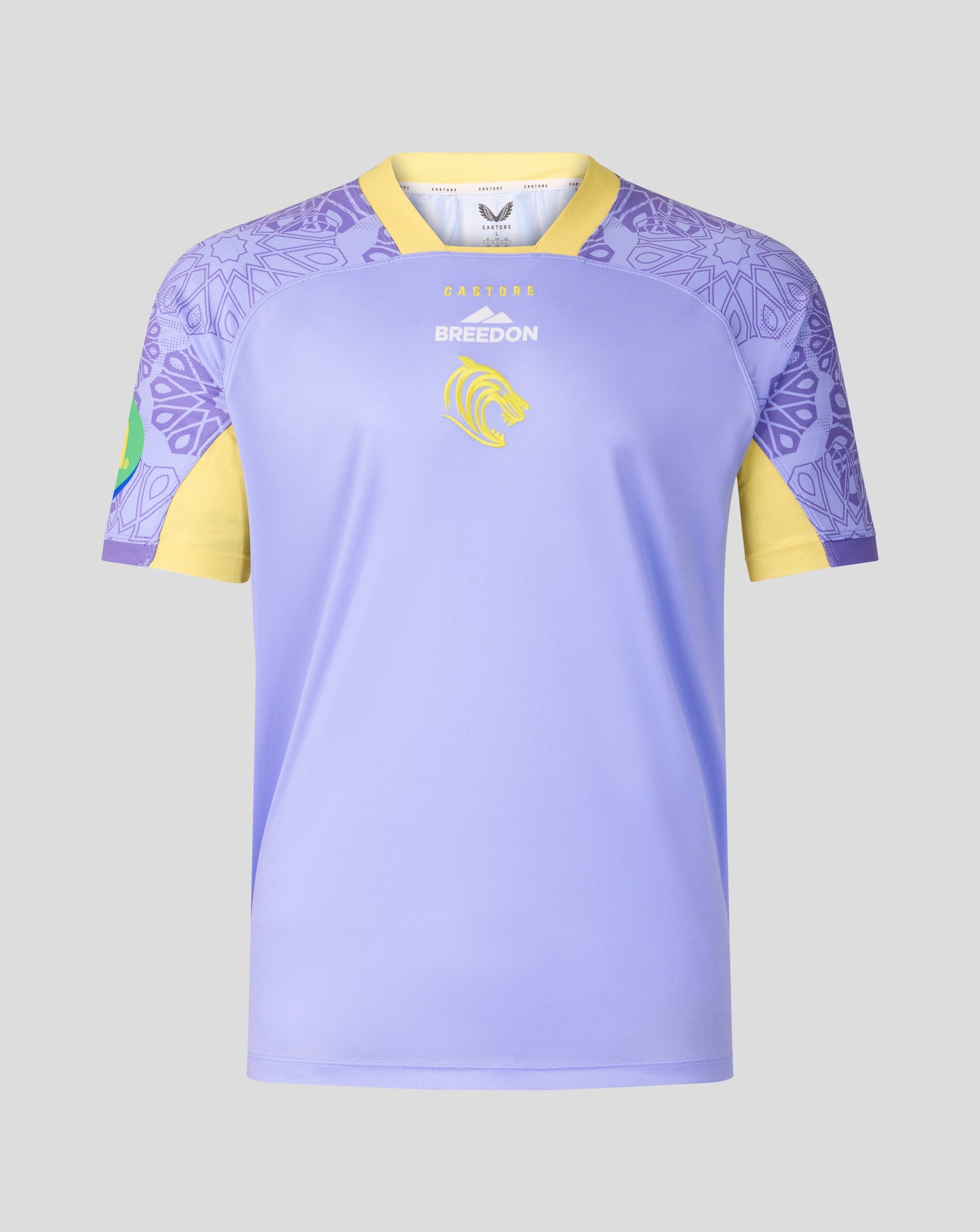 A short-sleeve soccer jersey in light purple with yellow sleeves and collar trim, featuring a purple mandala pattern on the shoulders and a yellow lion crest on the chest.