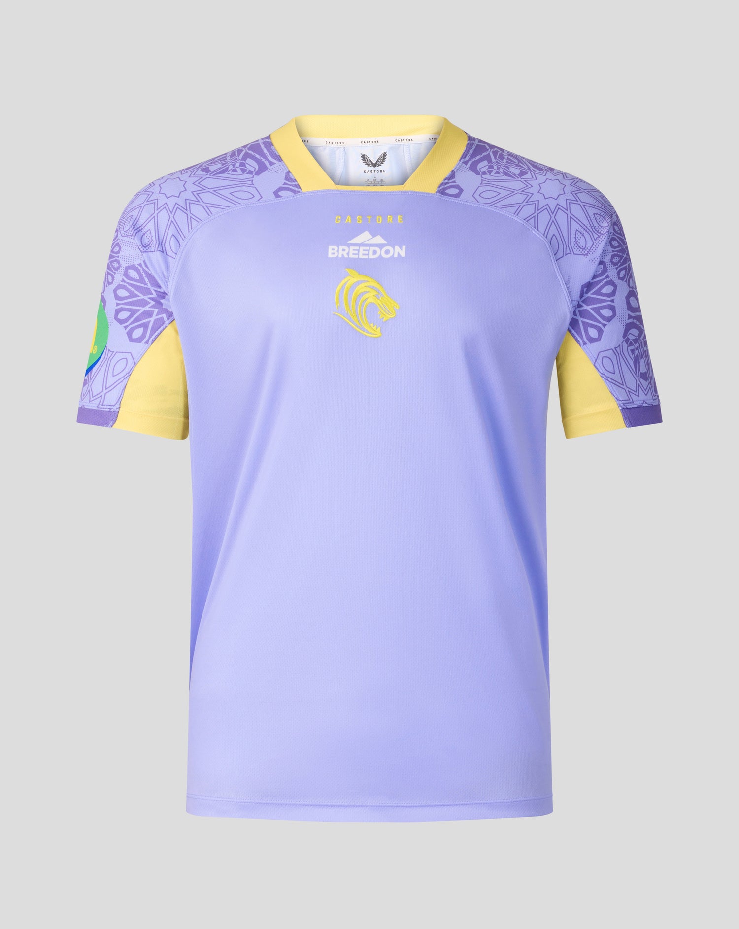 A short-sleeve soccer jersey in light purple with yellow sleeves and collar trim, featuring a purple mandala pattern on the shoulders and a yellow lion crest on the chest.