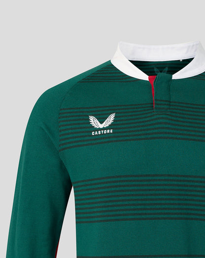 Close-up of a green long-sleeve rugby shirt with thin dark horizontal stripes, a white collar, a red inner placket, and a white Castore wing logo on the chest.
