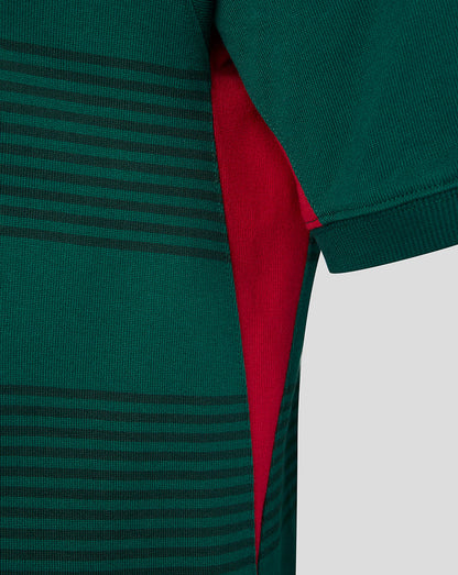 Close-up of a green ribbed knit garment with thin horizontal dark stripes and a bright red inner lining visible along the side slit.