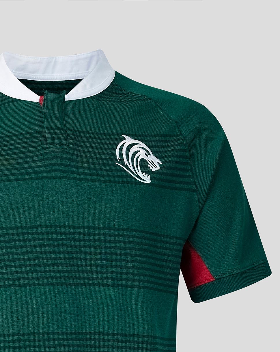 Close-up of a dark green rugby jersey with horizontal dark stripes, a white collar, a white animal head crest on the chest, and a red accent panel on the sleeve, shown against a light gray background.