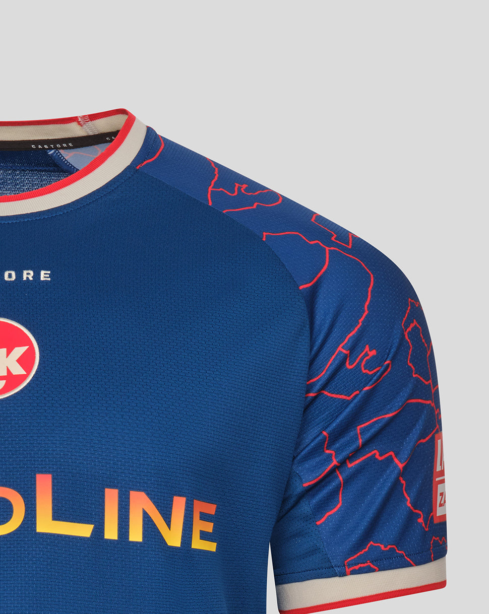 Close-up of the blue away shirt showing red map pattern on the shoulder, crest on the chest, and the orange gradient NOVO sponsor across the front.