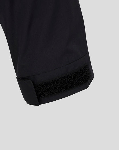 Close-up of a black garment cuff with a hook-and-loop fastening closure, shown against a light gray background.
