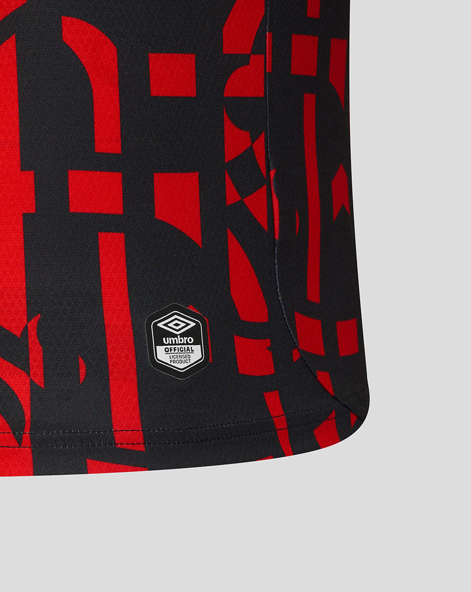 Close-up of a black athletic shorts leg featuring a bold red abstract geometric pattern and a white Umbro logo patch near the hem, set against a light gray background.