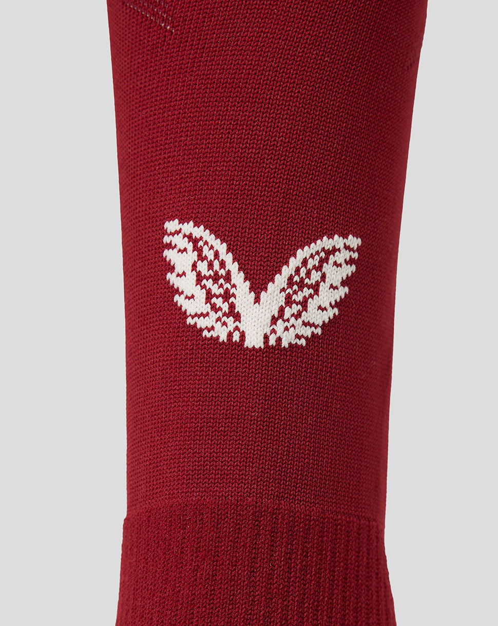 A close-up of a red knit sock featuring a white knit Castore motif on the side, set against a solid light gray background.