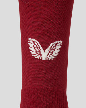 A close-up of a red knit sock featuring a white knit Castore motif on the side, set against a solid light gray background.