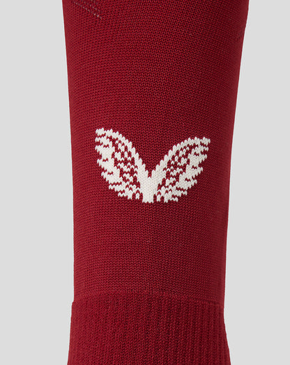A close-up of a red knit sock featuring a white knit Castore motif on the side, set against a solid light gray background.
