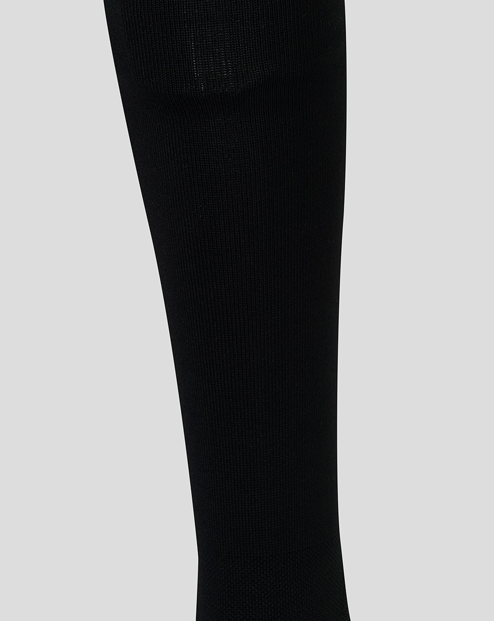 Close-up of a black ribbed knit sock, shown against a light gray background.